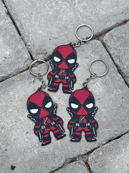 Three Deadpool keychains on a textured stone surface. Ideal accessory for Marvel fans who love Deadpool's humor and charm.